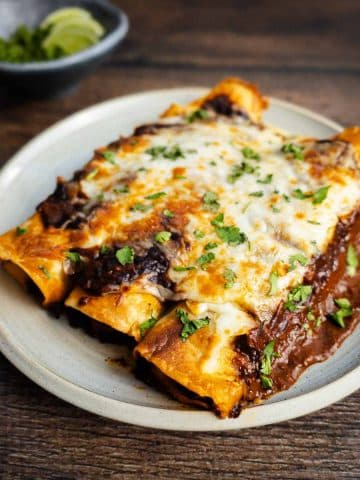 A plate of chicken thigh enchiladas on a wooden table topped with homemade red enchilada sauce, and melty cheese.