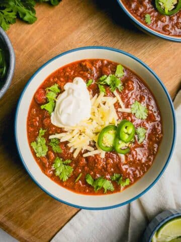 A bowl of Beef and Chorizo chili on a wooden cutting board.