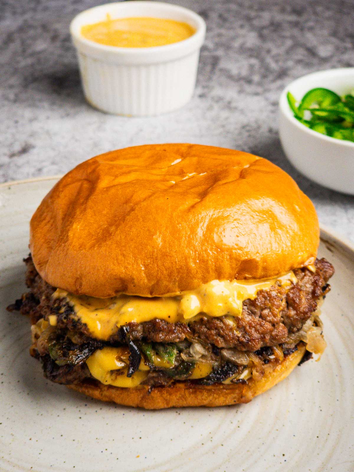A smash burger with onion, jalapeño, and pickled okra burger sauce on a plate.