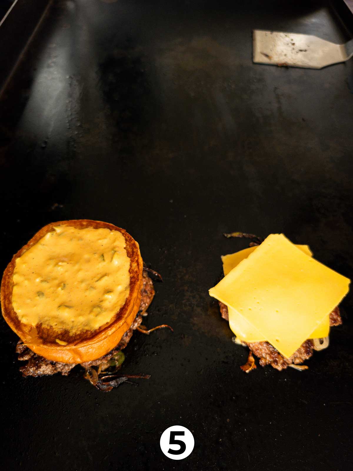 Prepared buns placed on top of burger patties on a hot griddle.