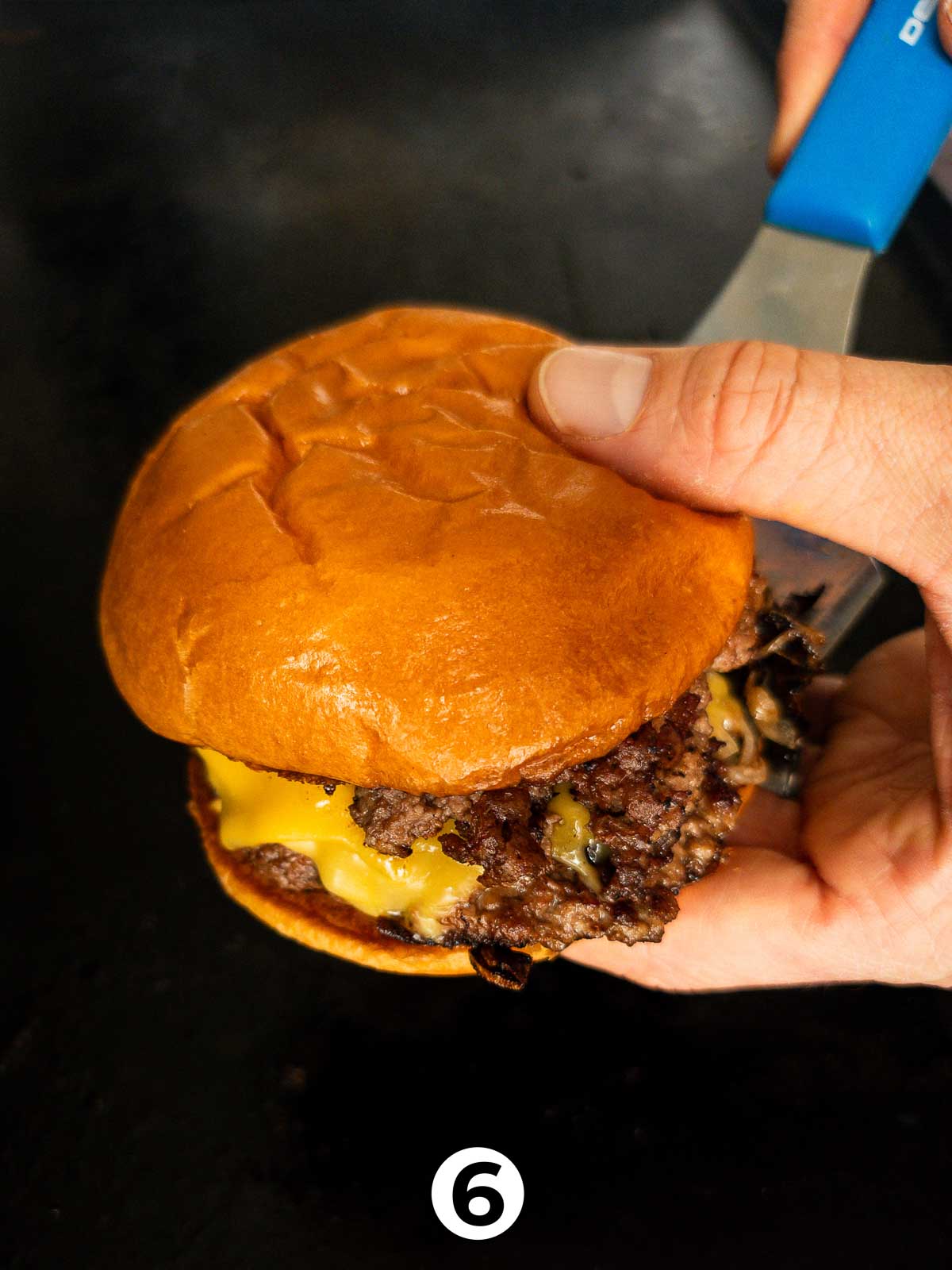 A spatula assembling a double smash burger with onion an jalapeño.
