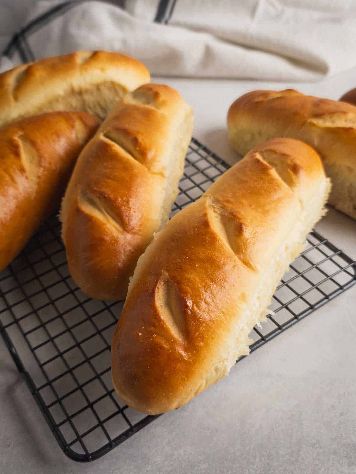 Freshly baked handmade sub rolls cooling on a wire rack.