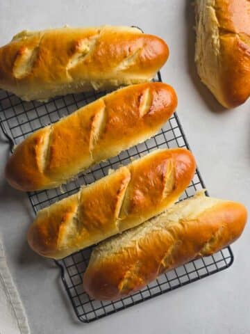Freshly baked handmade sub rolls cooling on a wire rack.