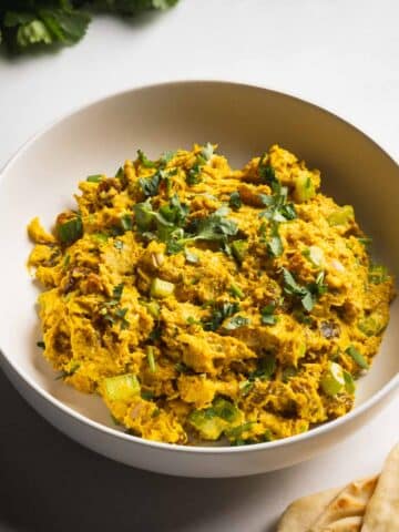 A bowl of curry chicken salad with rotisserie chicken served with naan and cliantro.